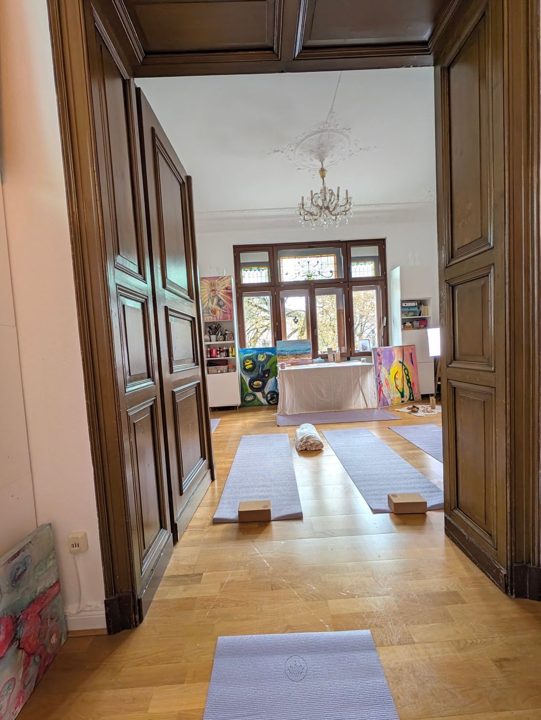 Blick durch eine alte Flügeltür in den hellen Atelierraum mit Yogamatten und Kronleuchter