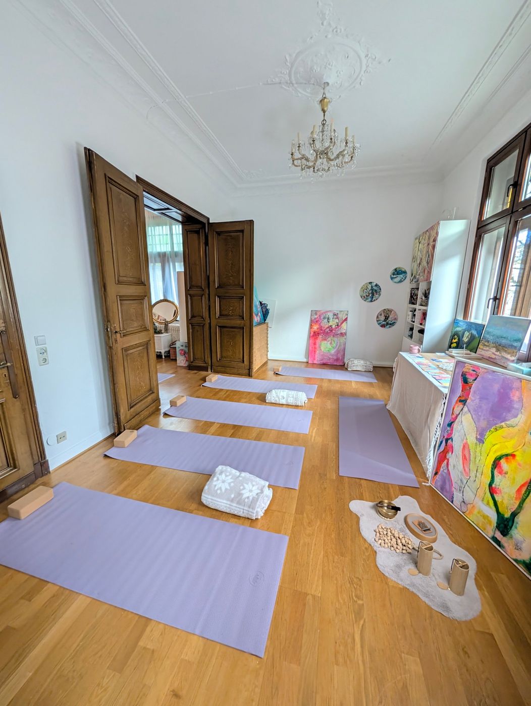 Yogamatten mit Korkblöcken und Decken im Atelier, daneben bunte Gemälde