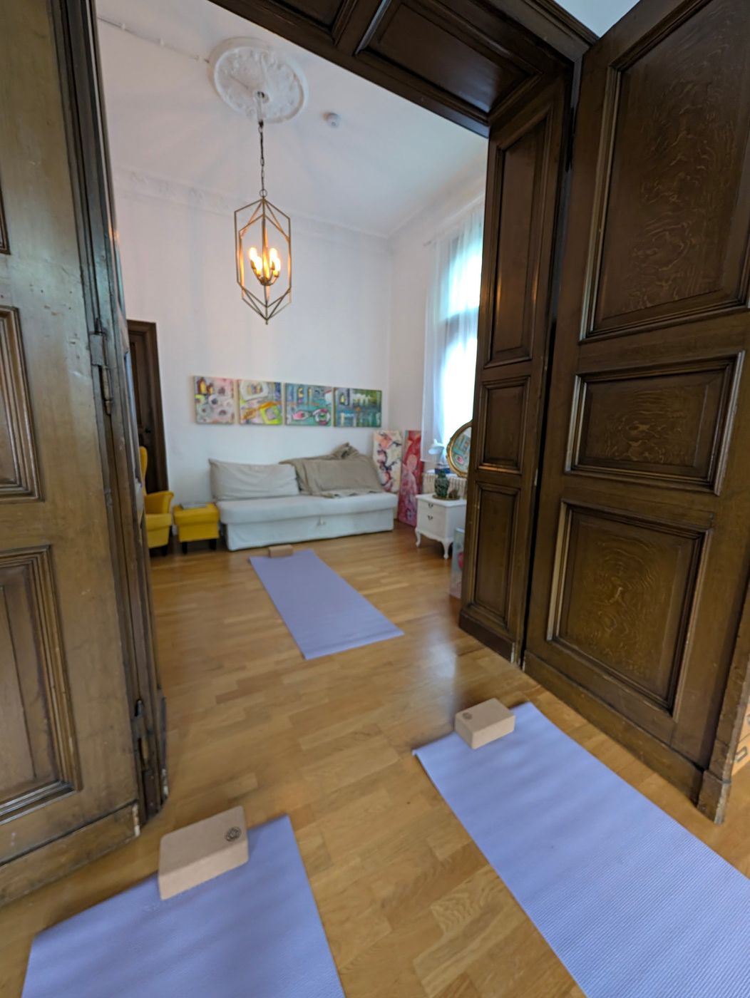 Blick durch eine Flügeltür in einen ruhigen Nebenraum mit Sofa und Bildern